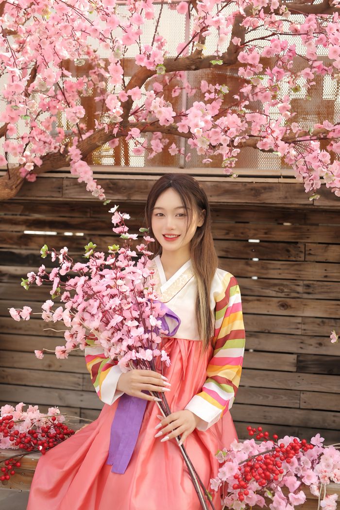 A young Korean woman in traditional hanbok sitting among vibrant cherry blossoms.