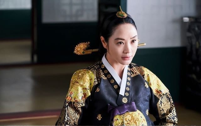 A royal figure in traditional Korean dress in a dim palace interior